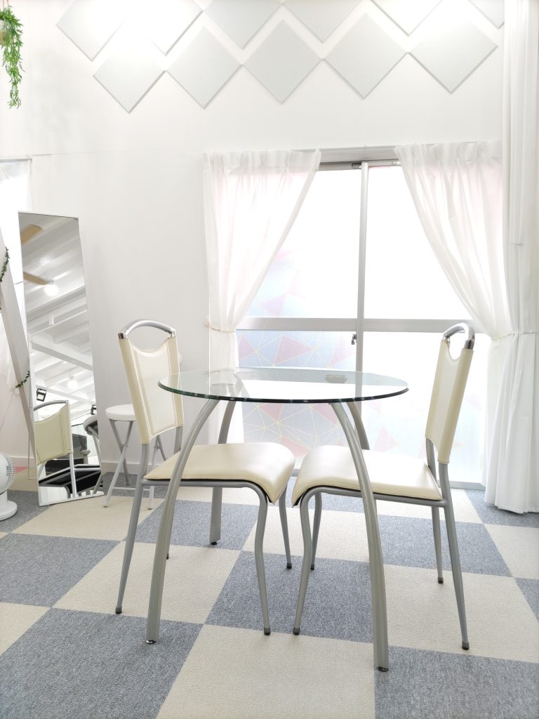 白いカーテンと明るい窓を背景にした、新しいガラスのテーブルと椅子。