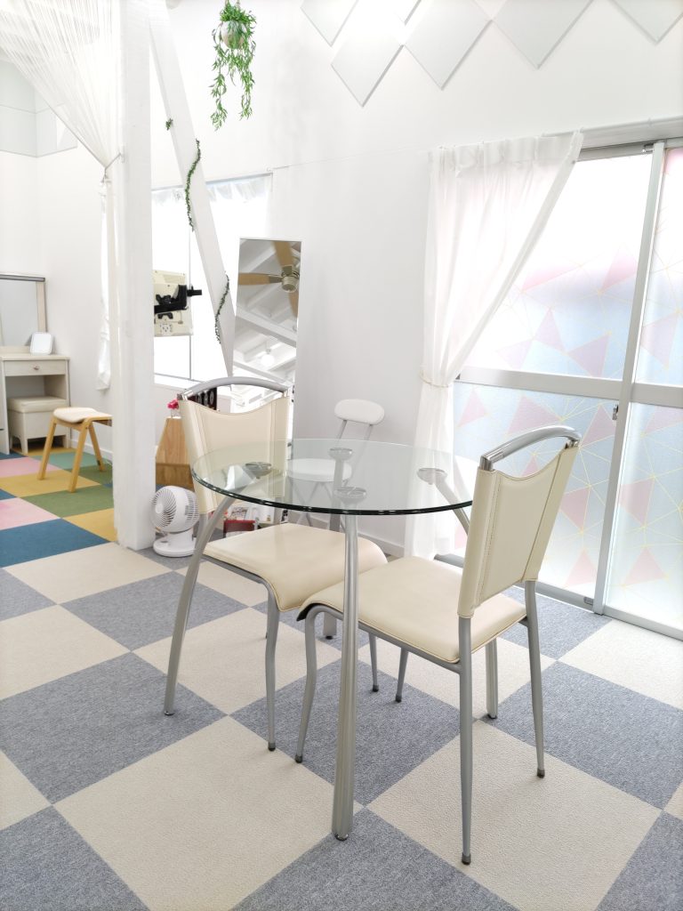 明るい室内で、透明なガラスのテーブルと二脚の椅子が並んだ様子。